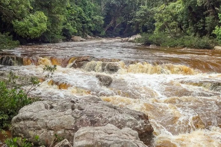 The cascade at Lata Berkoh running high and brown over its rock shelf, with granite boulders in the foreground