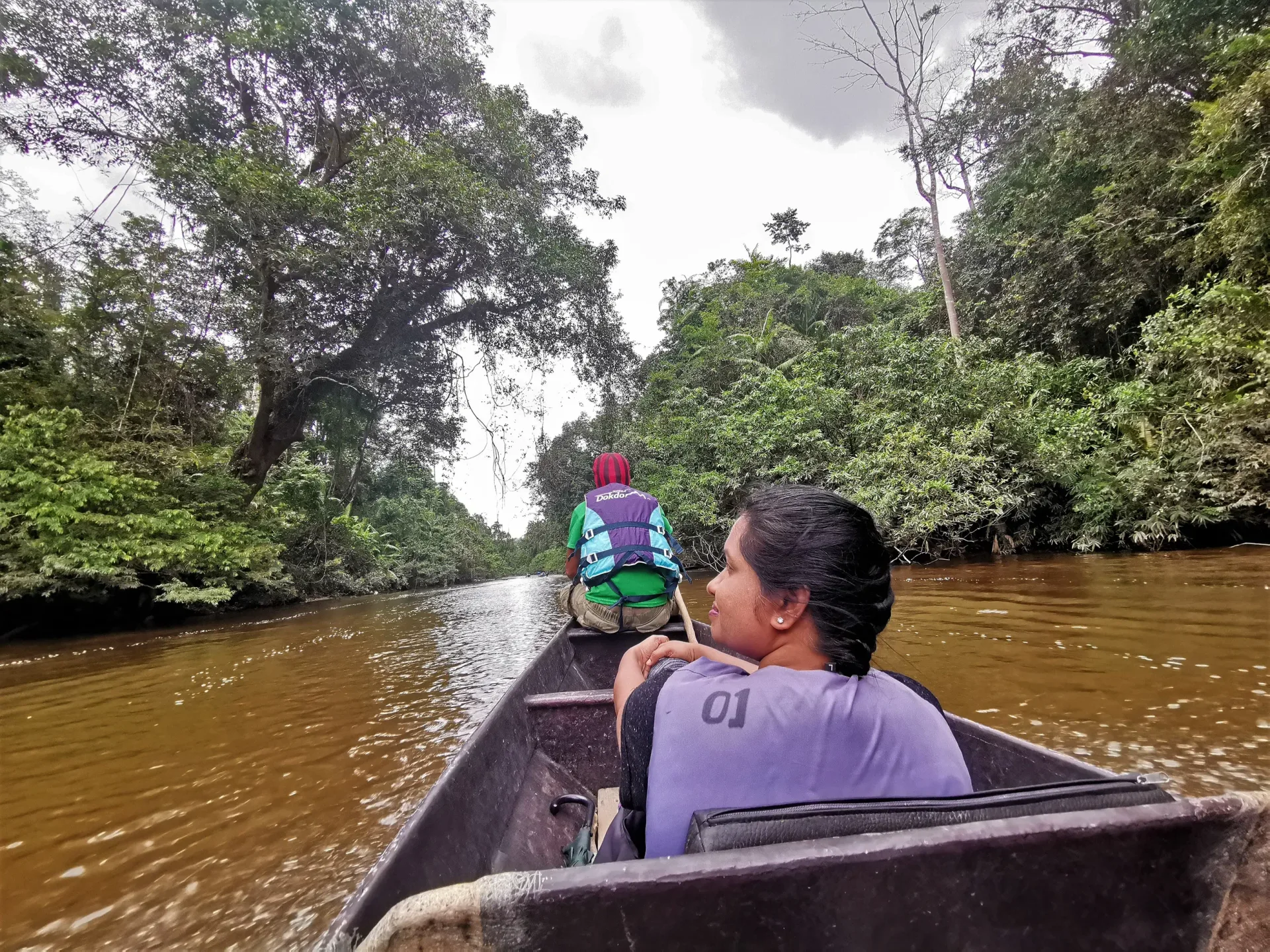 The view forward from inside a longboat heading upriver, with the bowman ahead and forest closing in on both banks