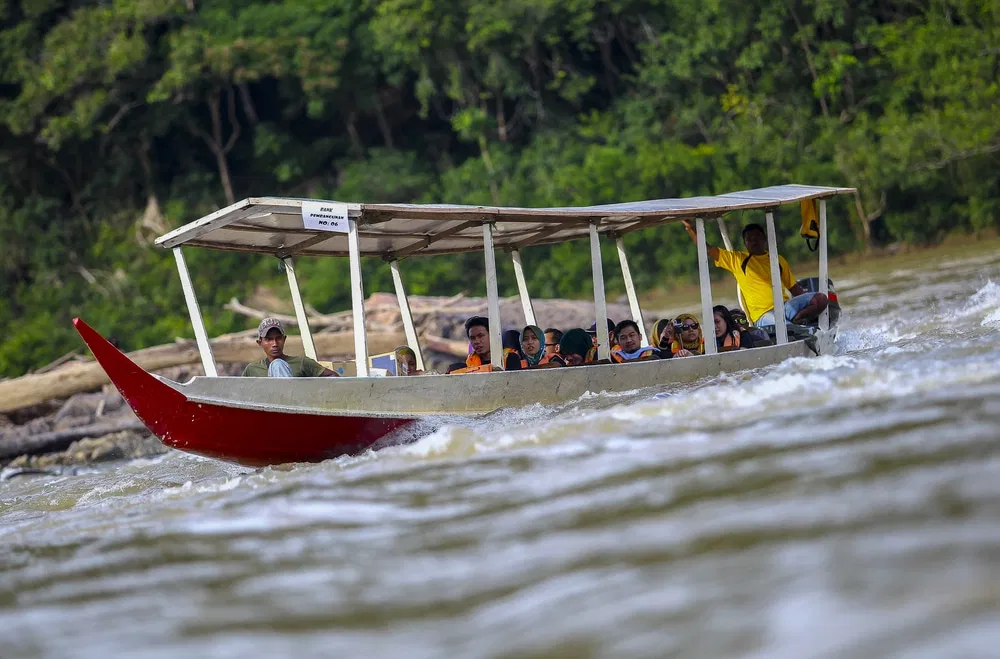 A roofed passenger longboat driving through white water with everyone aboard in life jackets